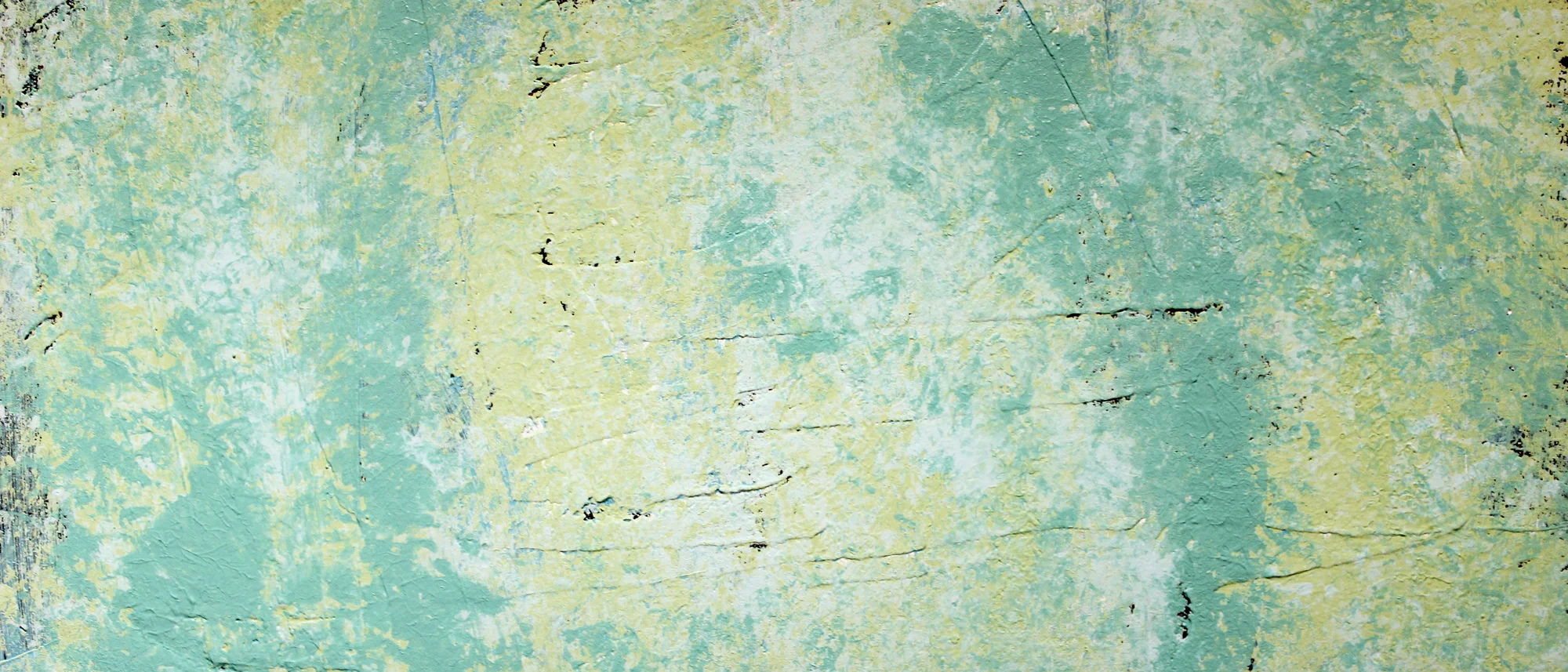 Nahaufnahme einer strukturierten Wand mit einer verwitterten, grün-gelblichen Farboberfläche. Die raue, ungleichmäßige Textur zeigt Abnutzungsspuren, Risse und dunklere Kratzer.